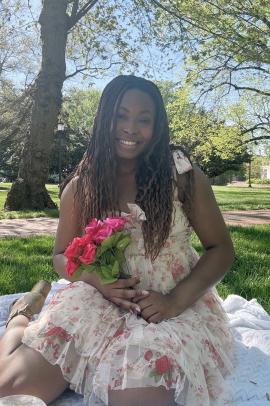 Layomi Omole sitting outside on a white blanket holding red and pink roses in her hands