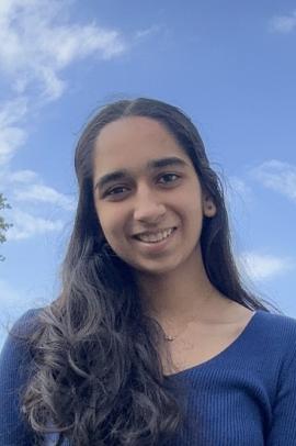 Anahat standing and smiling outdoors against the daytime sky with a few clouds
